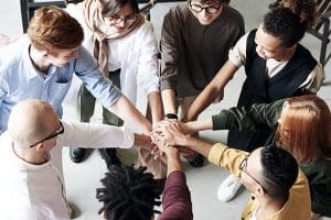 Personen, die im Kreis stehen und die Hände aufeinanderlegen, als Zeichen für Zusammenhalt